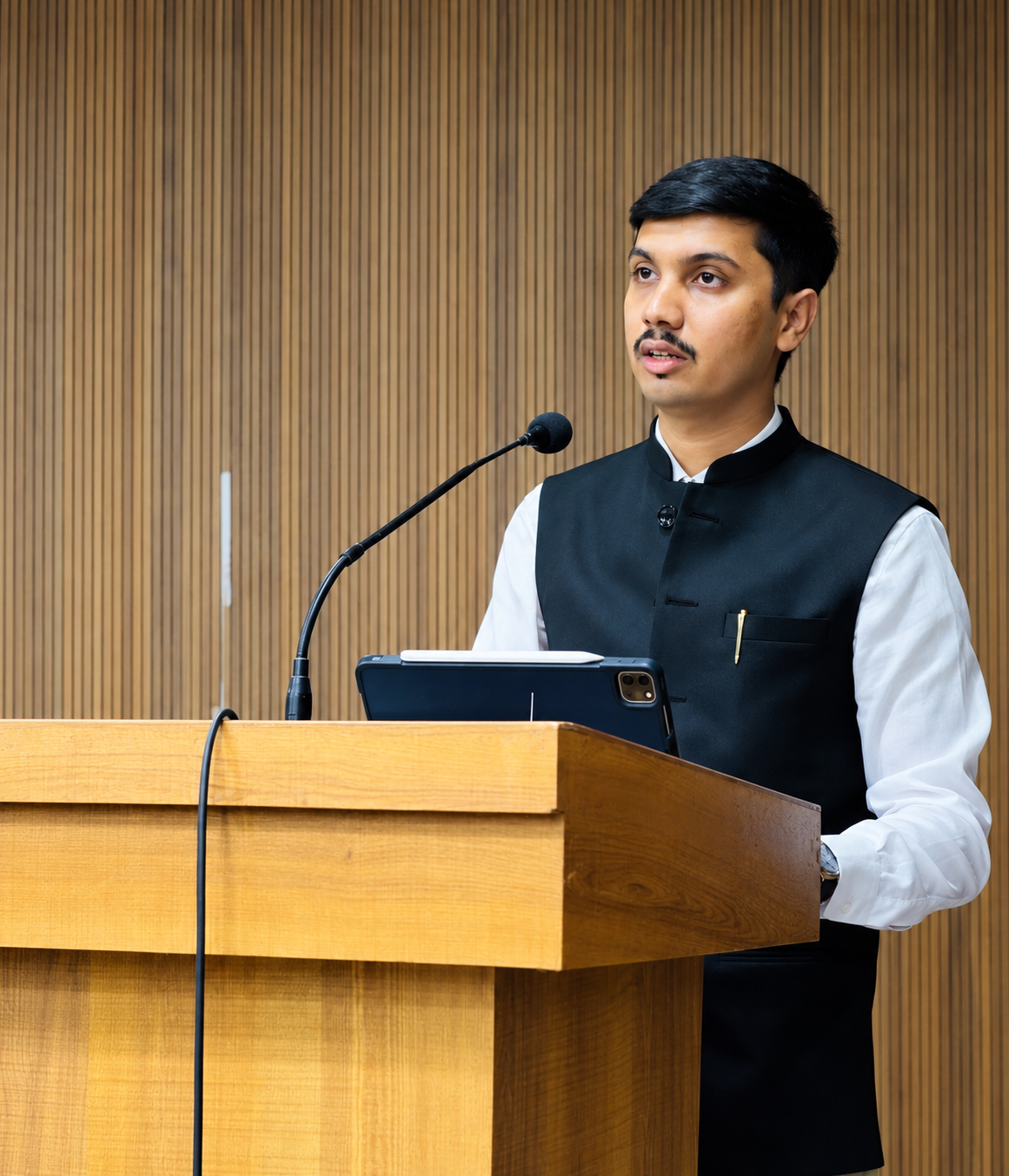 Advocate Dev Kella speaking at a wooden lectern